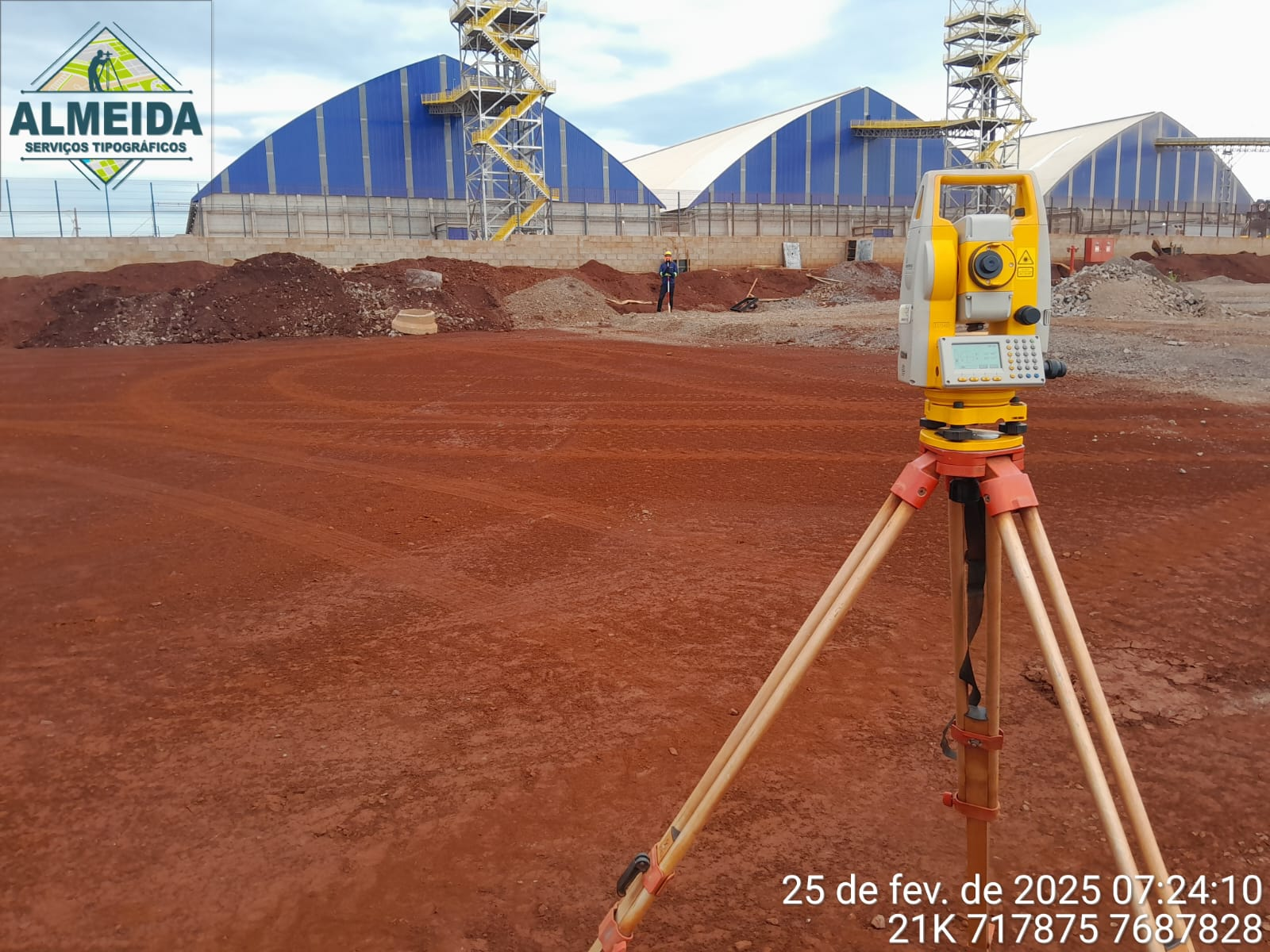 Estação total posicionada em área ampla de terraplenagem e implantação industrial.